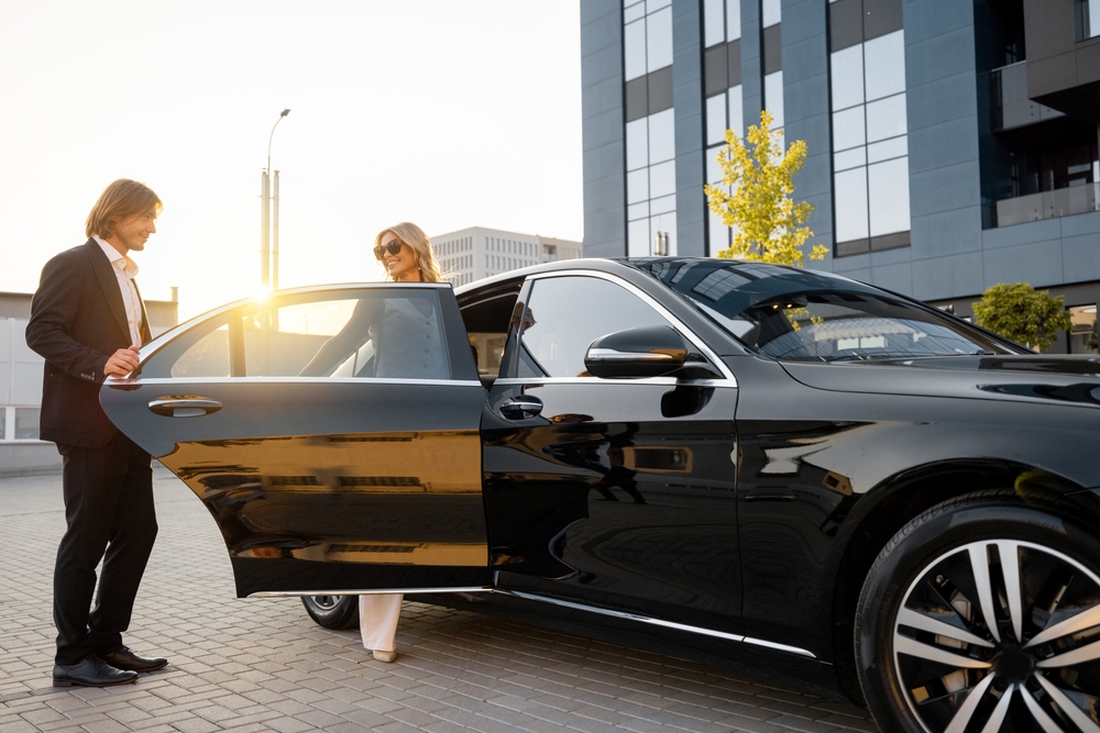A man in a suit holding open a car door as a woman steps out
