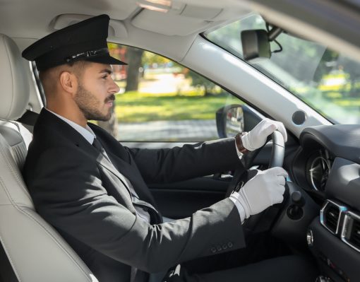 A chauffeur with a hat and gloves behind the wheel of a car